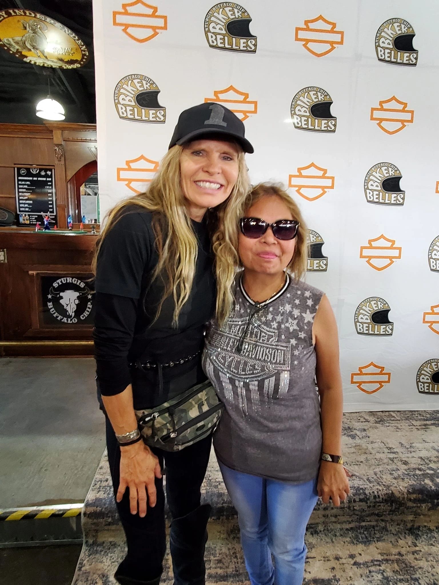 Two women smiling at a biker rally event with branded Marie's backdrop.